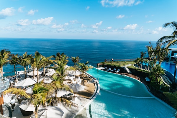 A palm-lined swimming pool overlooking a blue coastline
